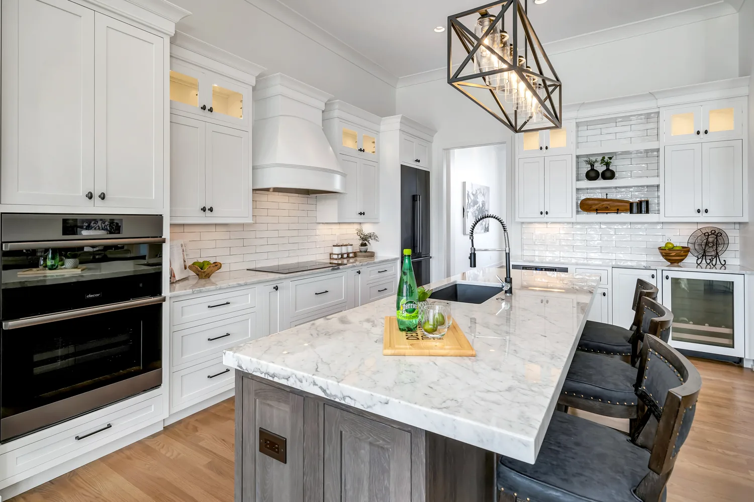 White kitchen with a marble island, brass lighting and wood flooring
